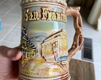 Könnte beinhalten: Ein Bierkrug aus Keramik mit einem braunen und weißen Design, das eine Straßenbahn und den Text "San Francisco" und "Chinatown" zeigt.