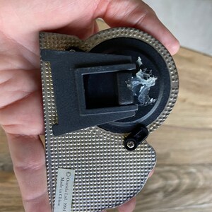 May include: A silver-colored metal protractor with a black plastic handle and a black knob. The protractor has a textured surface and the text "&copy; Oneida Ltd 1991 Made in China" is printed on the side.