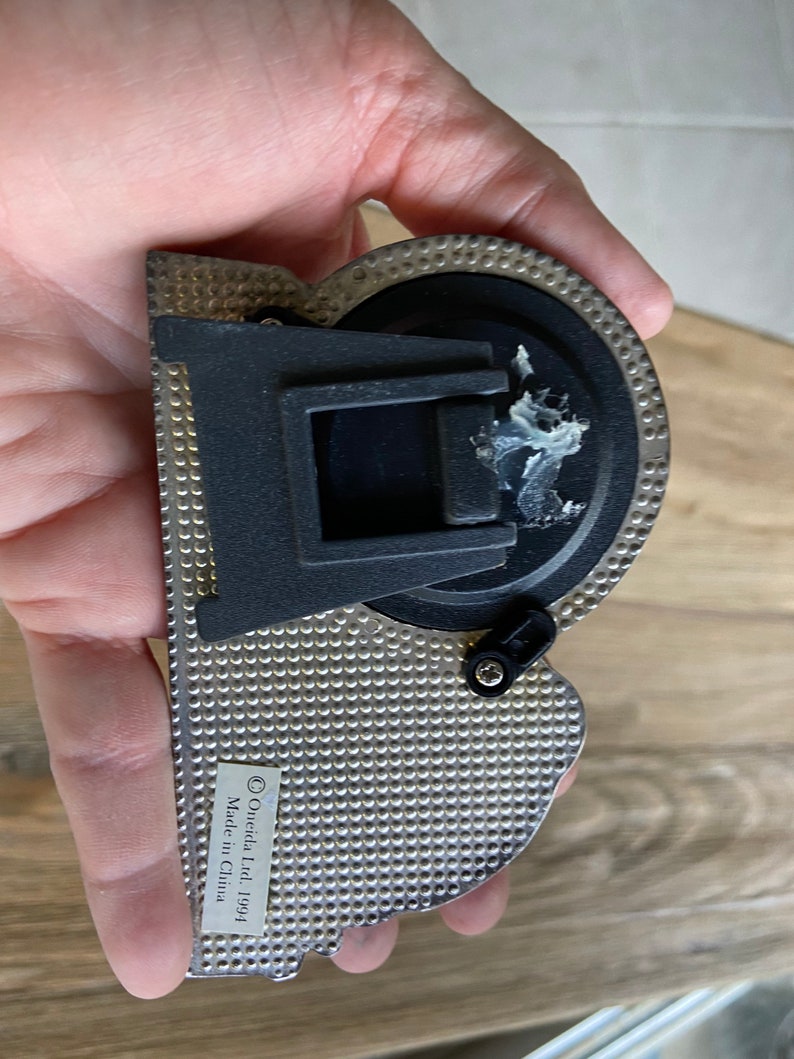 May include: A silver-colored metal protractor with a black plastic handle and a black knob. The protractor has a textured surface and the text "&copy; Oneida Ltd 1991 Made in China" is printed on the side.