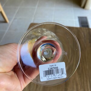 May include: Close-up of the base of a clear glass wine glass with a blue rim. A white sticker with black text and a barcode reads "York / 0 C387000 0 7873781468 9 Made in Czech Republic".