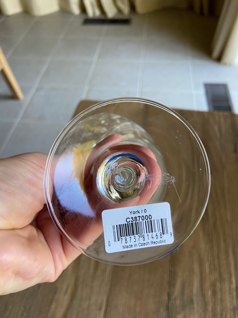 May include: Close-up of the base of a clear glass wine glass with a blue rim. A white sticker with black text and a barcode reads "York / 0 C387000 0 7873781468 9 Made in Czech Republic".