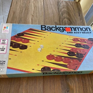 May include: A vintage Milton Bradley Backgammon game box with a blue background and the text "Backgammon and Acey-Deucy". The box features a colorful game board with black and red checkers and white dice.
