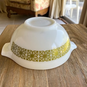 May include: White mixing bowl with a green floral pattern around the rim. The bowl has two handles on the sides.