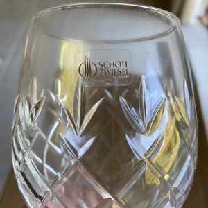 May include: A clear glass wine glass with a cut crystal design. The glass has a sticker on the bottom that reads "SCHOTT ZWIESEL TRIPLEX".