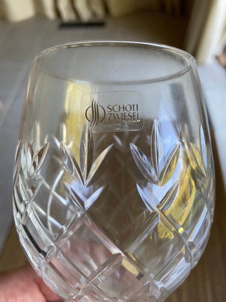 May include: A clear glass wine glass with a cut crystal design. The glass has a sticker on the bottom that reads "SCHOTT ZWIESEL TRIPLEX".