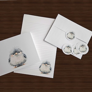 May include: A stationery set featuring white lined paper and matching envelopes decorated with a fluffy, grey, round bird illustration. The set includes a folded greeting card, a sheet of lined writing paper, and several circular stickers with the same bird.