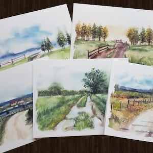 May include: Five watercolor paintings of country landscapes with dirt roads, fences, and trees. The paintings are on white paper and have a light blue background.