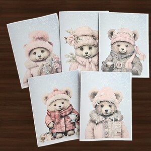 May include: Five greeting cards featuring watercolor illustrations of teddy bears in winter attire. Each bear wears a pink hat and coat, some with scarves or holding cups. The background is a light blue with snowflake accents.