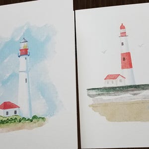 Peut inclure: Deux aquarelles de phares. La premi&egrave;re peinture montre un phare blanc avec un toit rouge et une petite maison rouge devant. La deuxi&egrave;me peinture montre un phare blanc avec une bande rouge et un toit rouge, sur une falaise surplombant une plage.