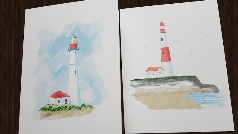 Peut inclure: Deux aquarelles de phares. La premi&egrave;re peinture montre un phare blanc avec un toit rouge et une petite maison rouge devant. La deuxi&egrave;me peinture montre un phare blanc avec une bande rouge et un toit rouge, sur une falaise surplombant une plage.