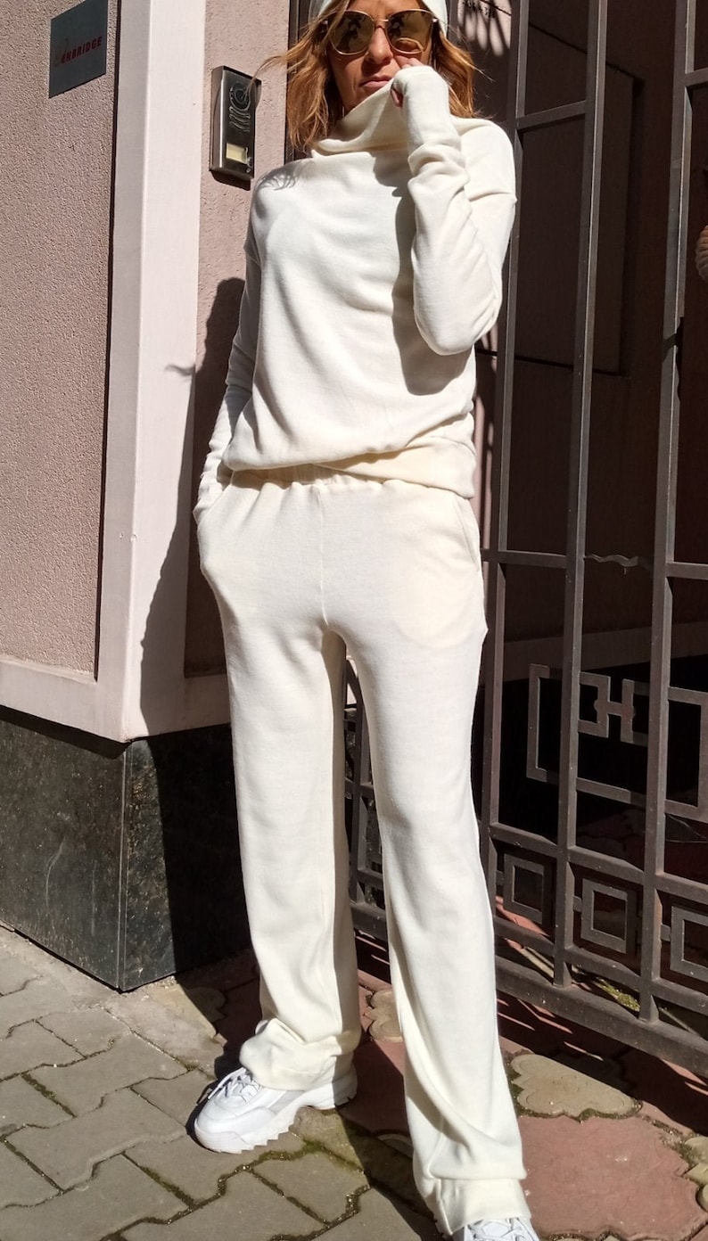 K&ouml;nnte beinhalten: Ein wei&szlig;er Strickpullover mit Rollkragen und eine passende Hose. Das Outfit wird mit einer wei&szlig;en M&uuml;tze und einer Sonnenbrille gestylt.