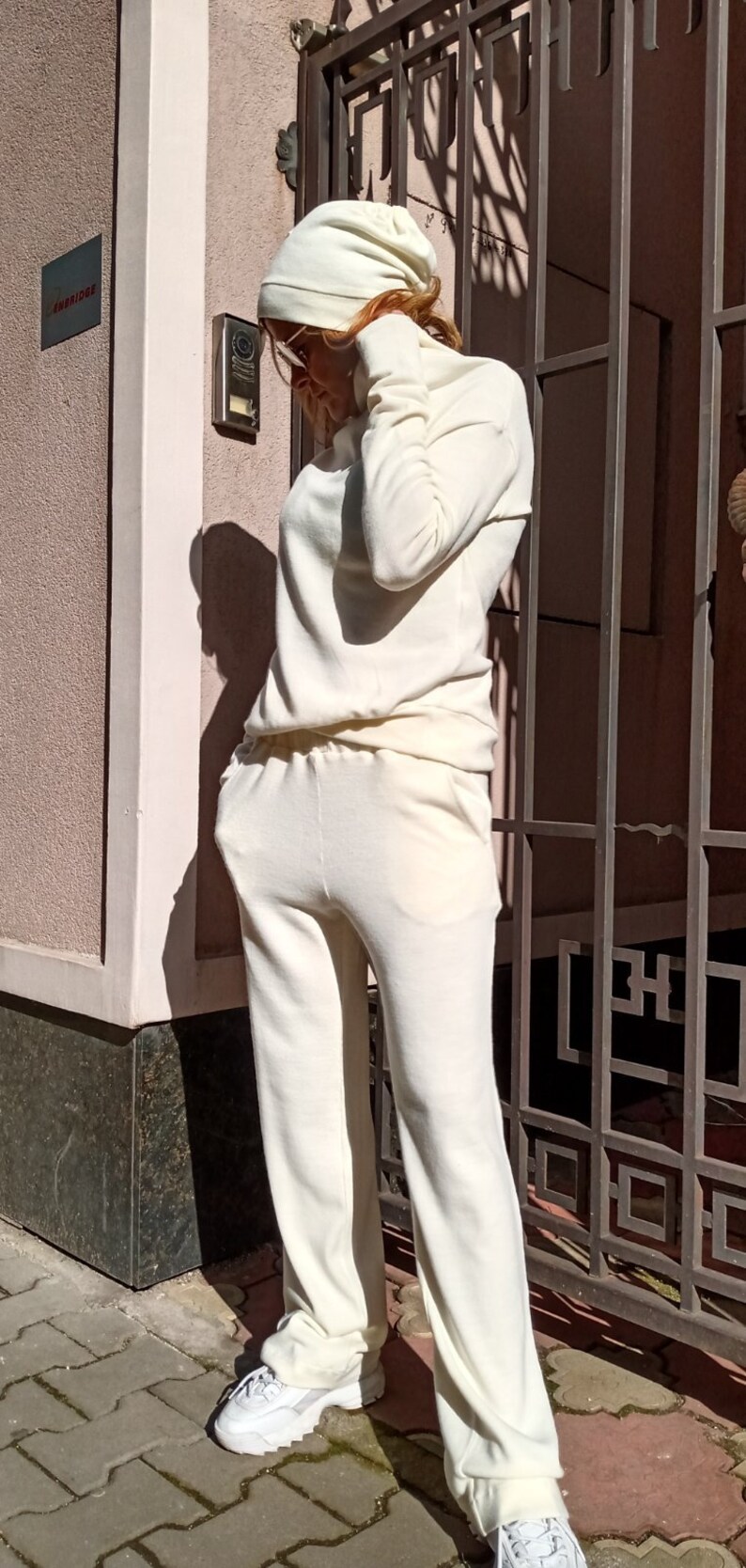 K&ouml;nnte beinhalten: Ein wei&szlig;er Strickpullover und eine passende Hose. Der Pullover hat einen Rollkragen und lange &Auml;rmel. Die Hose hat eine lockere Passform und ist an den Kn&ouml;cheln umgeschlagen. Die Person tr&auml;gt wei&szlig;e Turnschuhe.