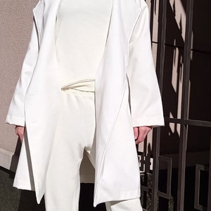K&ouml;nnte beinhalten: Ein wei&szlig;er Langarmmantel mit einem wei&szlig;en Rollkragenpullover und einer wei&szlig;en Hose. Die Person tr&auml;gt eine Sonnenbrille und eine wei&szlig;e M&uuml;tze.
