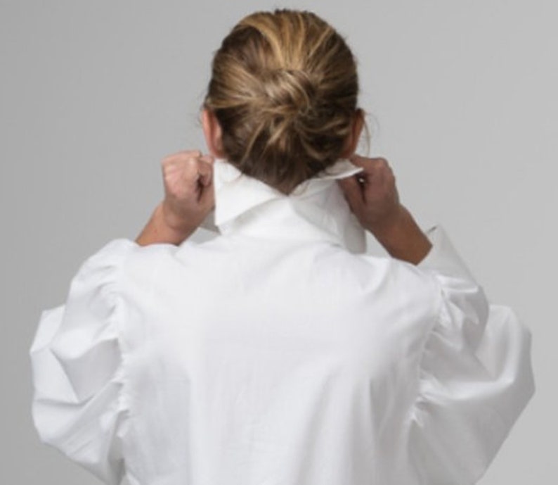 May include: A white collared shirt with puffed sleeves. The shirt is made of a soft, lightweight fabric.