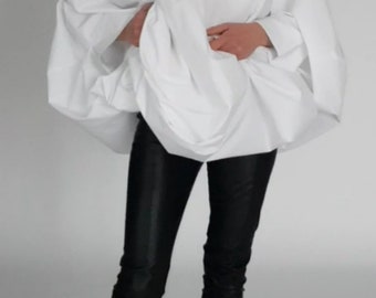 May include: A white oversized button-down shirt with long sleeves and a gathered waist. The shirt is worn with black pants and black heeled ankle boots.