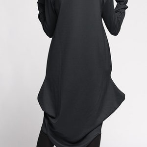 Op de afbeelding: Zwarte kap-tuniek met een lang, vloeiend ontwerp. De tuniek heeft een losse pasvorm en een geplooide zoom. Het model draagt zwarte panty's en zwarte schoenen.