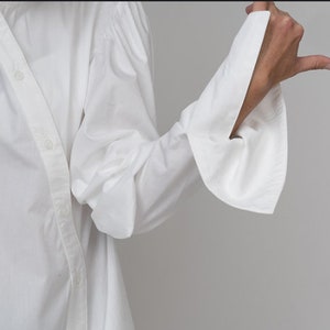 May include: A white long-sleeved shirt with a button-up front and large, gathered sleeves. The sleeves have a wide, flared cuff.