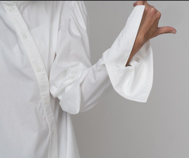 May include: A white long-sleeved shirt with a button-up front and large, gathered sleeves. The sleeves have a wide, flared cuff.