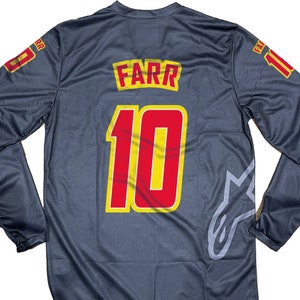May include: Dark grey long-sleeved jersey with the name "FARR" and the number "10" in red and yellow. The number "11" is on the right sleeve. The jersey has a grey star logo on the lower right side.