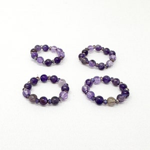 May include: Four amethyst gemstone bracelets with a mix of purple and light purple beads.