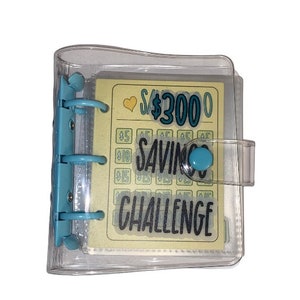 May include: A clear plastic binder with a yellow and blue card inside. The card has the text "$3000 Saving Challenge" on it.