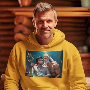 Puede incluir: Una sudadera con capucha amarilla con un estampado gráfico de dos hombres, uno con una corona y barba, sosteniendo un tridente. Los hombres están en una escena submarina azul.