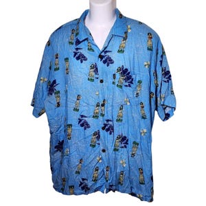 May include: Light blue Hawaiian shirt with a pattern of hula dancers, flowers, and leaves. The short-sleeved shirt has a button-down front and a collared neckline. The fabric has a textured appearance.