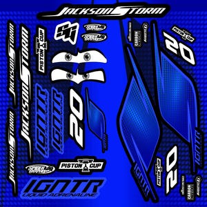 May include: A collection of blue and white racing car decals. The decals feature the text "JACKSON STORM", "IGNTR LIQUID ADRENALINE", "PISTON CUP", and the number "20". Additional graphics include stylized eyes and the "SPIDER TRAPHIX" logo.