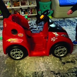 May include: A red toy car with black accents, a steering wheel, and silver wheels. The car features stickers with the number 95 and the word "RACING". A fun toy for children.