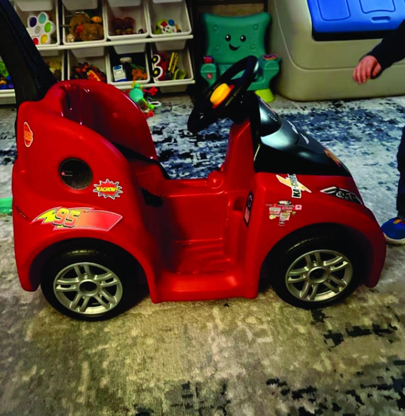 May include: A red toy car with black accents, a steering wheel, and silver wheels. The car features stickers with the number 95 and the word "RACING". A fun toy for children.