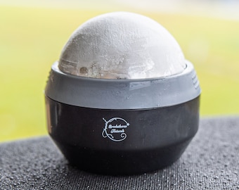 May include: A black and gray ice ball maker with a white ice ball inside. The ice ball maker has the text "Breakstone Naturals" on the side.