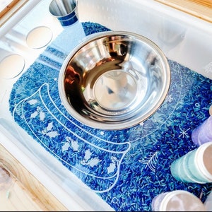 May include: A stainless steel bowl sits on a blue and white patterned mat filled with blue rice. The mat has a design of holly leaves and berries.
