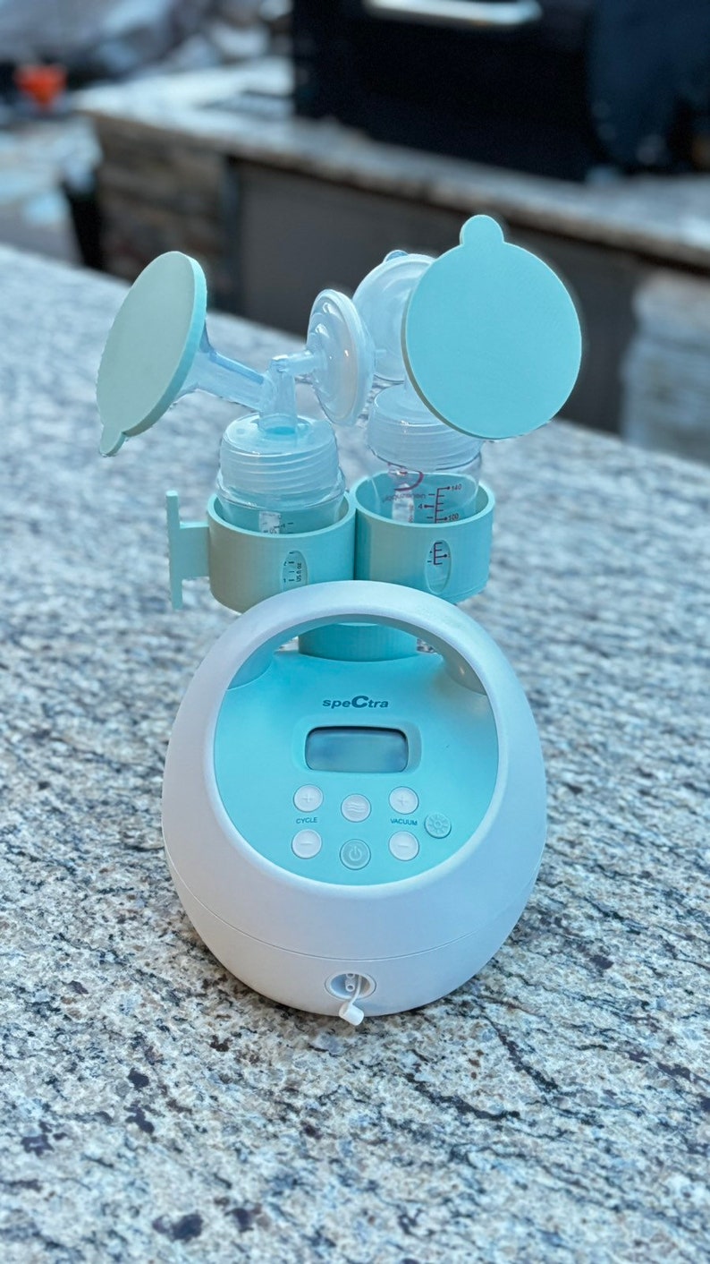May include: A white and light blue electric breast pump with a digital display and buttons labeled "cycle" and "vacuum". The pump has two bottles attached with blue caps.