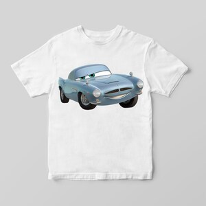 Puede incluir: Una camiseta blanca con un coche de dibujos animados azul impreso en la parte delantera. El coche tiene una cara sonriente y ojos verdes.
