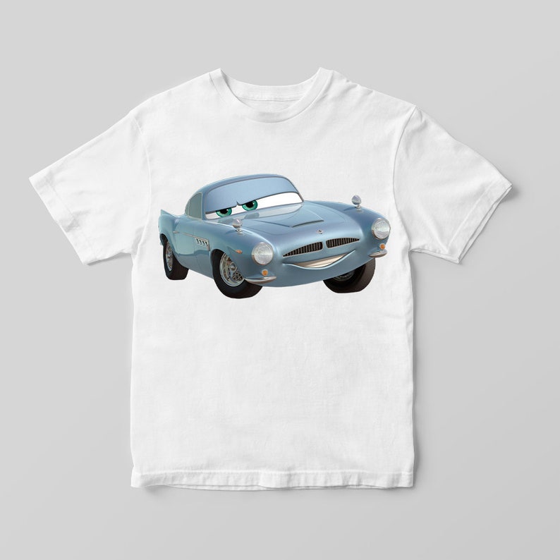 Puede incluir: Una camiseta blanca con un coche de dibujos animados azul impreso en la parte delantera. El coche tiene una cara sonriente y ojos verdes.