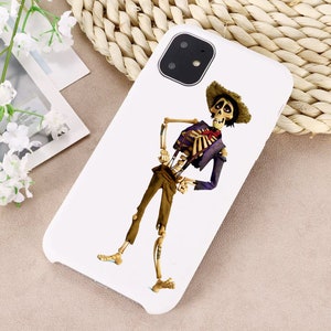 Puede incluir: Carcasa de tel&eacute;fono blanca con una imagen de dibujos animados de un esqueleto con una camisa morada, pantalones marrones y un sombrero de paja. El esqueleto sonr&iacute;e y lleva una corbata de lazo roja.