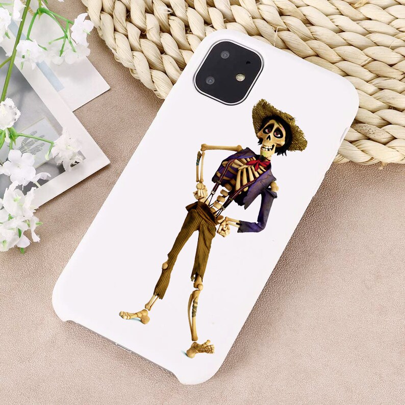 Puede incluir: Carcasa de tel&eacute;fono blanca con una imagen de dibujos animados de un esqueleto con una camisa morada, pantalones marrones y un sombrero de paja. El esqueleto sonr&iacute;e y lleva una corbata de lazo roja.