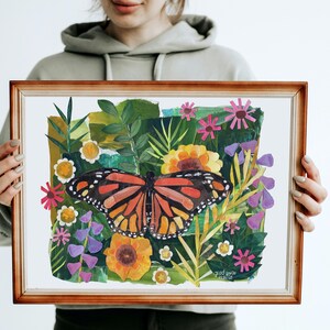 May include: A rectangular wooden frame containing a collage-style artwork of a monarch butterfly centered among various green leaves and colorful flowers in shades of yellow, pink, and purple. The text "glad you're here" is visible in the bottom right.
