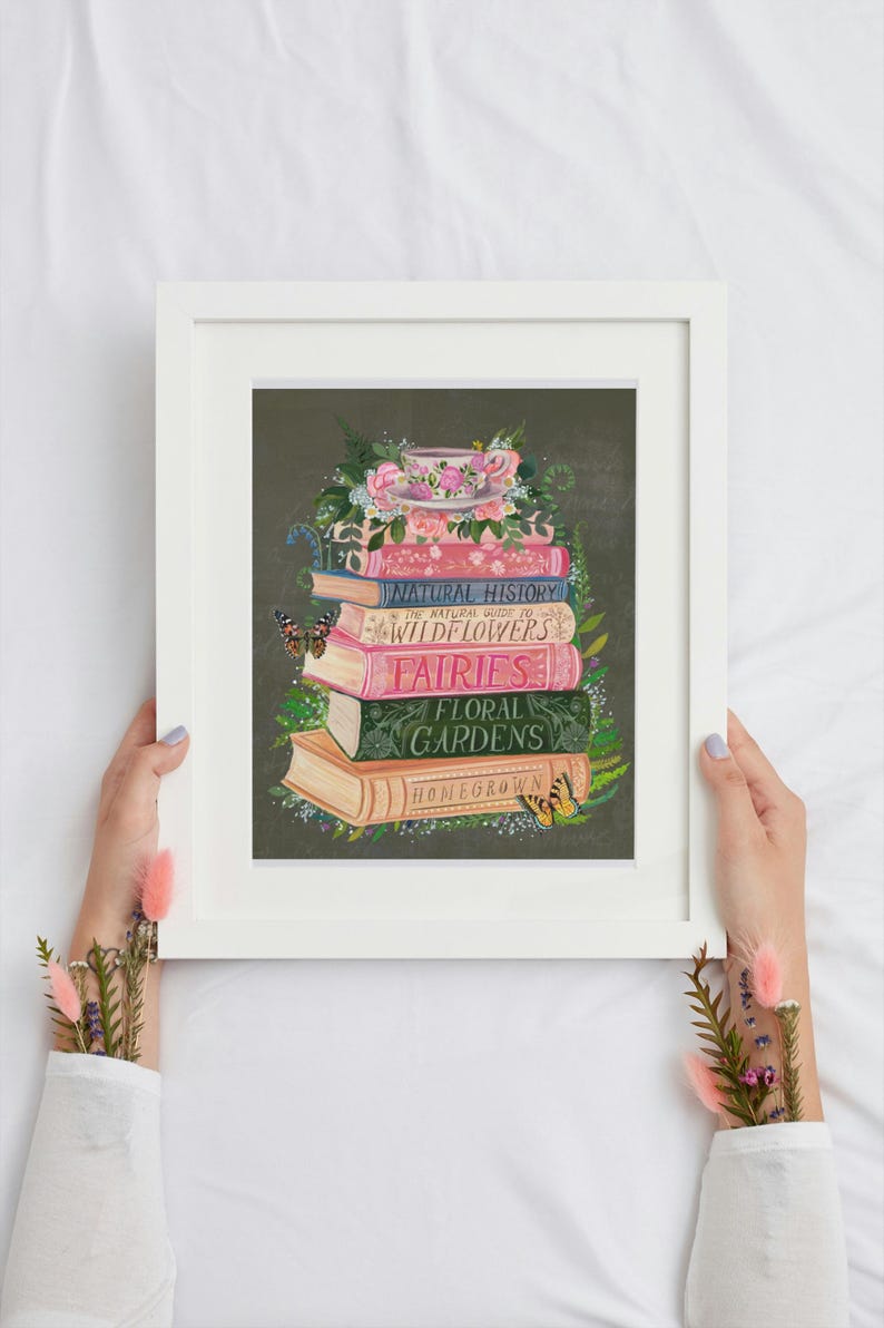 K&ouml;nnte beinhalten: Ein Stapel alter B&uuml;cher mit floralen Illustrationen und Titeln wie "Naturgeschichte", "Wildblumen", "Feen", "Blumen G&auml;rten" und "Eigenanbau". Eine Teetasse mit rosa Blumen steht oben auf dem Stapel.