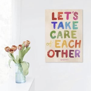 May include: A rectangular art print with the words "LET'S TAKE CARE of EACH OTHER" in colorful, playful lettering. The print is displayed on a white wall, with a vase of tulips in front of it.