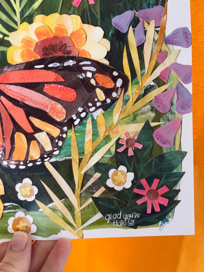May include: A paper collage artwork featuring a large monarch butterfly with orange and black wings, surrounded by yellow, purple, and white flowers and green foliage. The text "glad you're Here co." is printed in white near the bottom right corner.