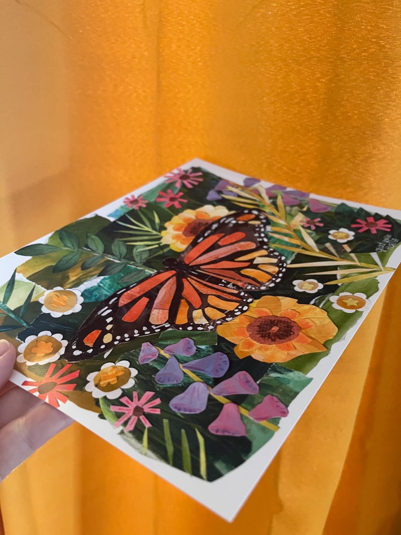 May include: A square art print featuring a central monarch butterfly with orange and black wings surrounded by a collage of green leaves, yellow sunflowers, small white flowers with gold centers, and purple bell-shaped blossoms on a dark background.