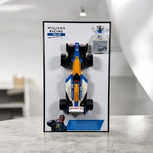 May include: A framed Williams Racing FW14B Formula 1 car model made of colorful building blocks. The model is blue, yellow, and white, with black wheels. The frame includes the Williams Racing logo and a picture of Nigel Mansell.