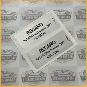 Puede incluir: Dos pegatinas rectangulares blancas con la palabra "RECARO" en negrita negra. Debajo, se lee "RECARO Pole Position 2003 KBA 91288". Las pegatinas están sobre un fondo con gráficos de coches y el texto "STICKERS FOR CAR".