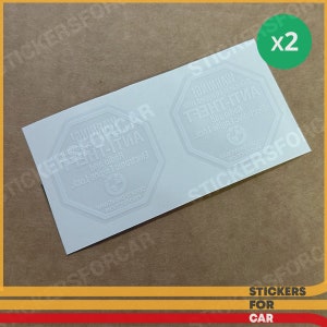 May include: Two white warning stickers with the text "WARNING! This car is equipped with electronic engine and radio anti-theft" in a white octagon shape with a BMW logo in the center. The stickers are on a white background.