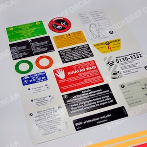 Könnte beinhalten: Ein Satz von 14 schwarzen und weißen Autoaufklebern mit verschiedenen Warnungen und Anweisungen. Die Aufkleber enthalten Text in Deutsch und Englisch, wie z. B. "Airbag", "Achtung", "Attention" und "Batterie".