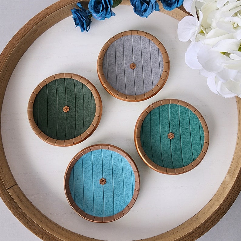 Pu&ograve; includere: Quattro sottobicchieri rotondi con un bordo in legno e un design centrale di assi di legno. I sottobicchieri sono in tonalit&agrave; di grigio, verde e blu.