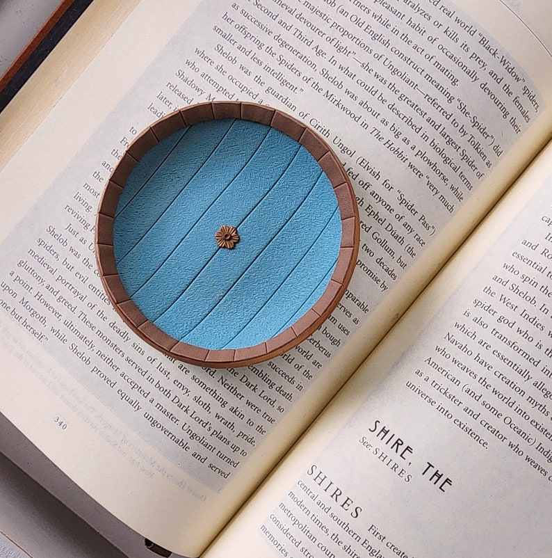 Pu&ograve; includere: Una replica in miniatura della porta blu della Contea ne Il Signore degli Anelli. La porta &egrave; fatta di argilla e ha una cornice in legno marrone. La porta &egrave; appoggiata su un libro con testo sulla storia della Contea.