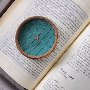 Pu&ograve; includere: Una porta verde turchese con una cornice marrone, che ricorda l'ingresso di una tana di hobbit. La porta &egrave; su un libro con il testo "Shelob era la guardiana di Cirith Ungol (elfico per "Passo del Ragno")" visibile.