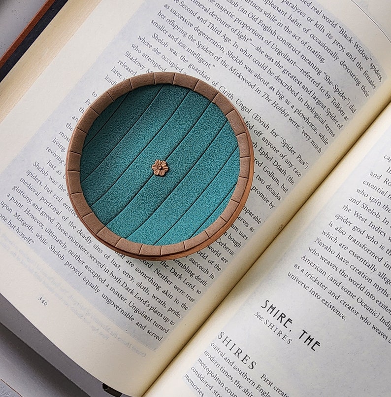 Pu&ograve; includere: Una porta verde turchese con una cornice marrone, che ricorda l'ingresso di una tana di hobbit. La porta &egrave; su un libro con il testo "Shelob era la guardiana di Cirith Ungol (elfico per "Passo del Ragno")" visibile.
